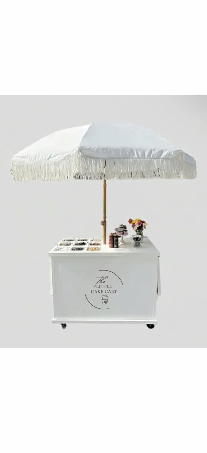 The Little Cake Cart branded white cart with fringe umbrella and toppings station