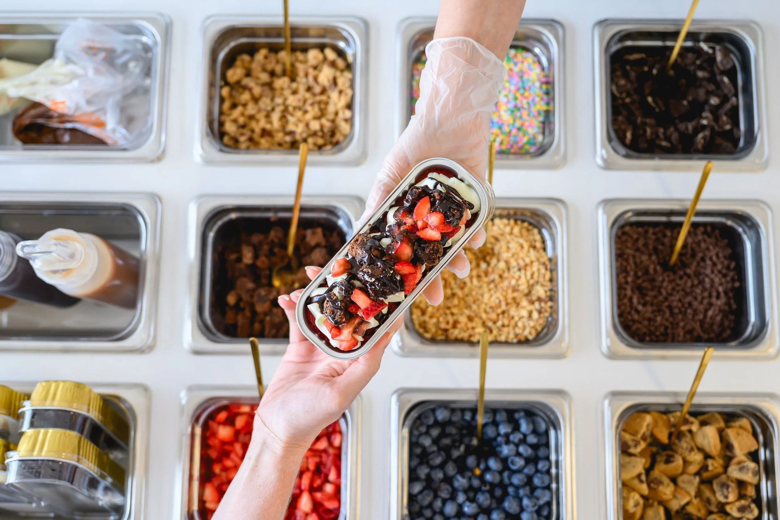 Hand plating a strawberry-chocolate mini dessert boat over a tray of toppings
